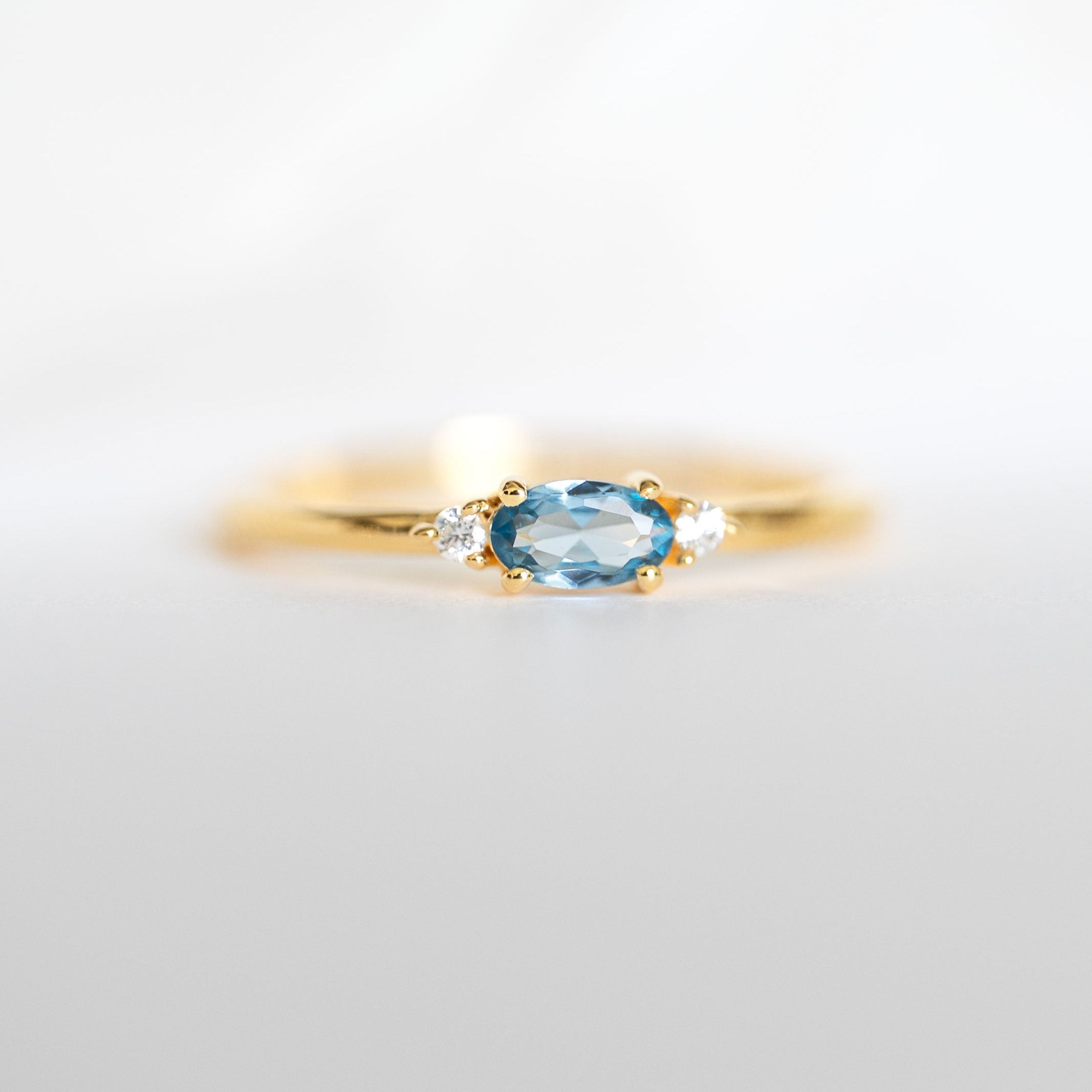 A gold vermeil dainty stacking ring with a marquise cut aquamarine center stone and two smaller clear stones on the sides, branded 'VEATGE'.