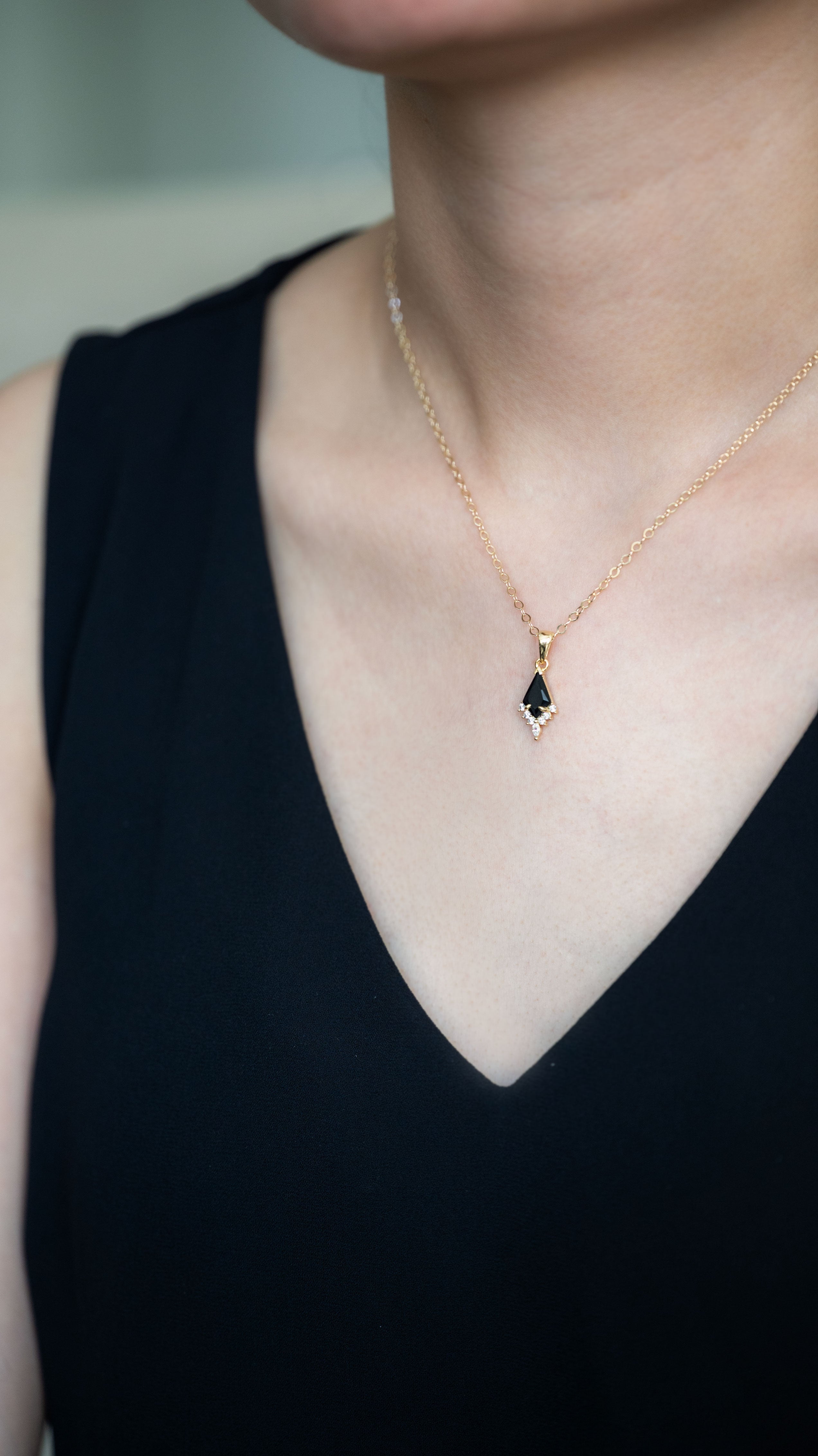 Person wearing a gold necklace with a green gemstone pendant against a neutral background