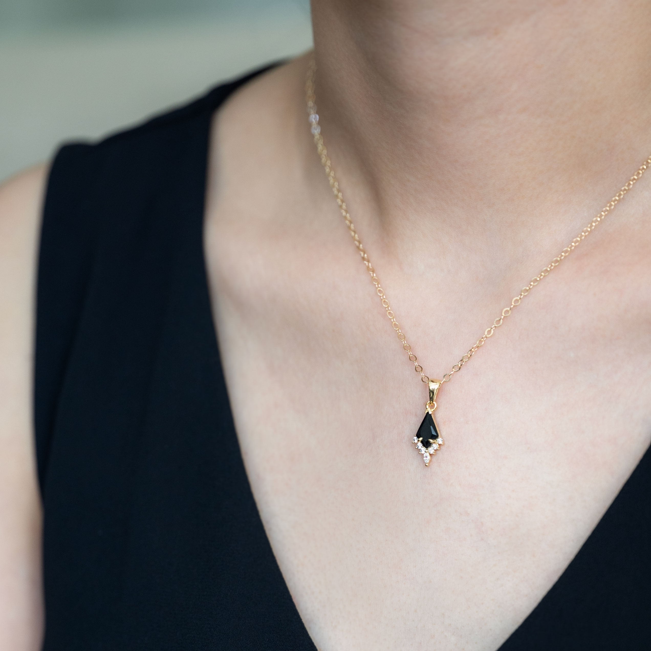 Person wearing a gold necklace with a green gemstone pendant against a neutral background
