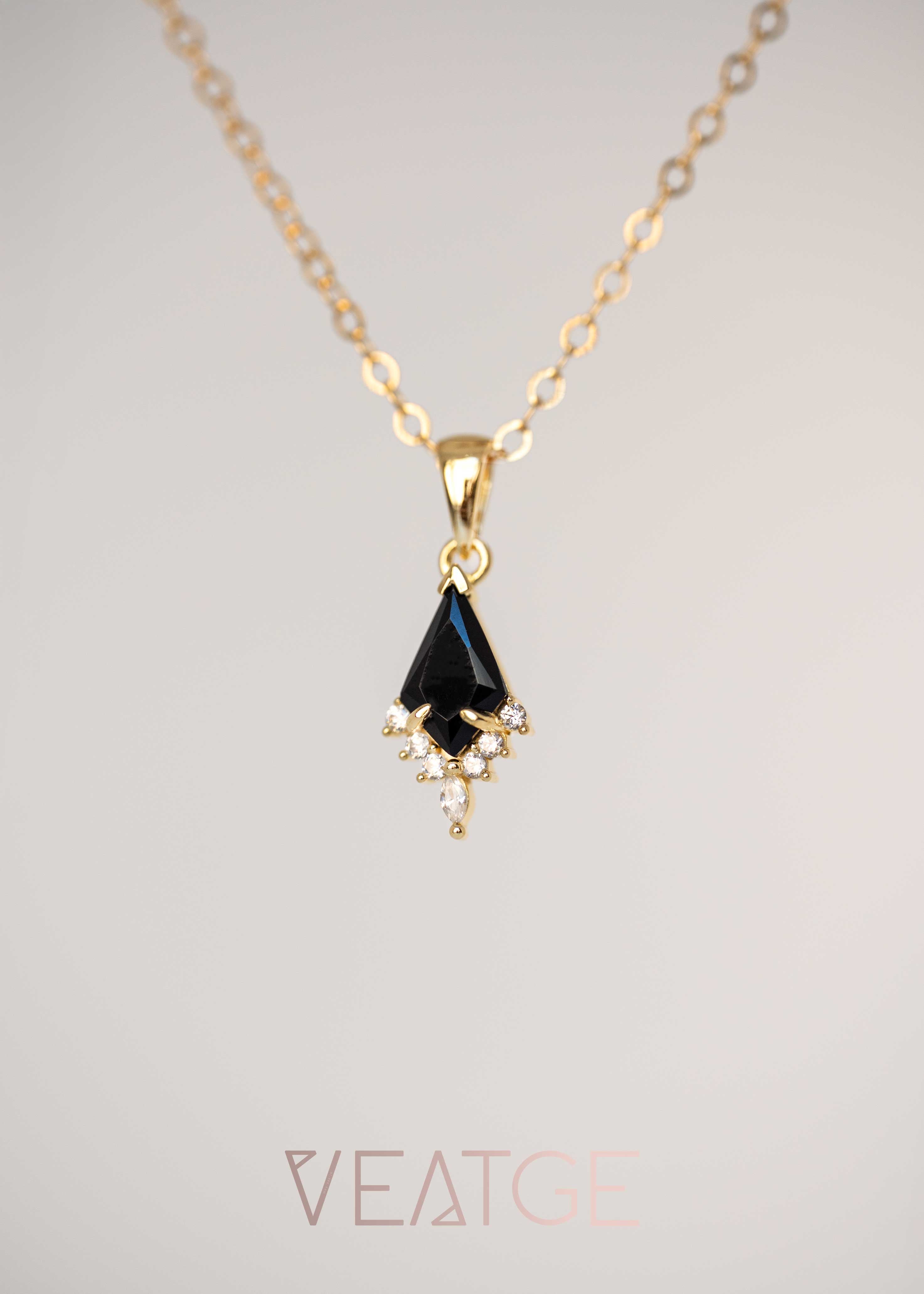 Gold necklace with a black teardrop pendant on a light gray background