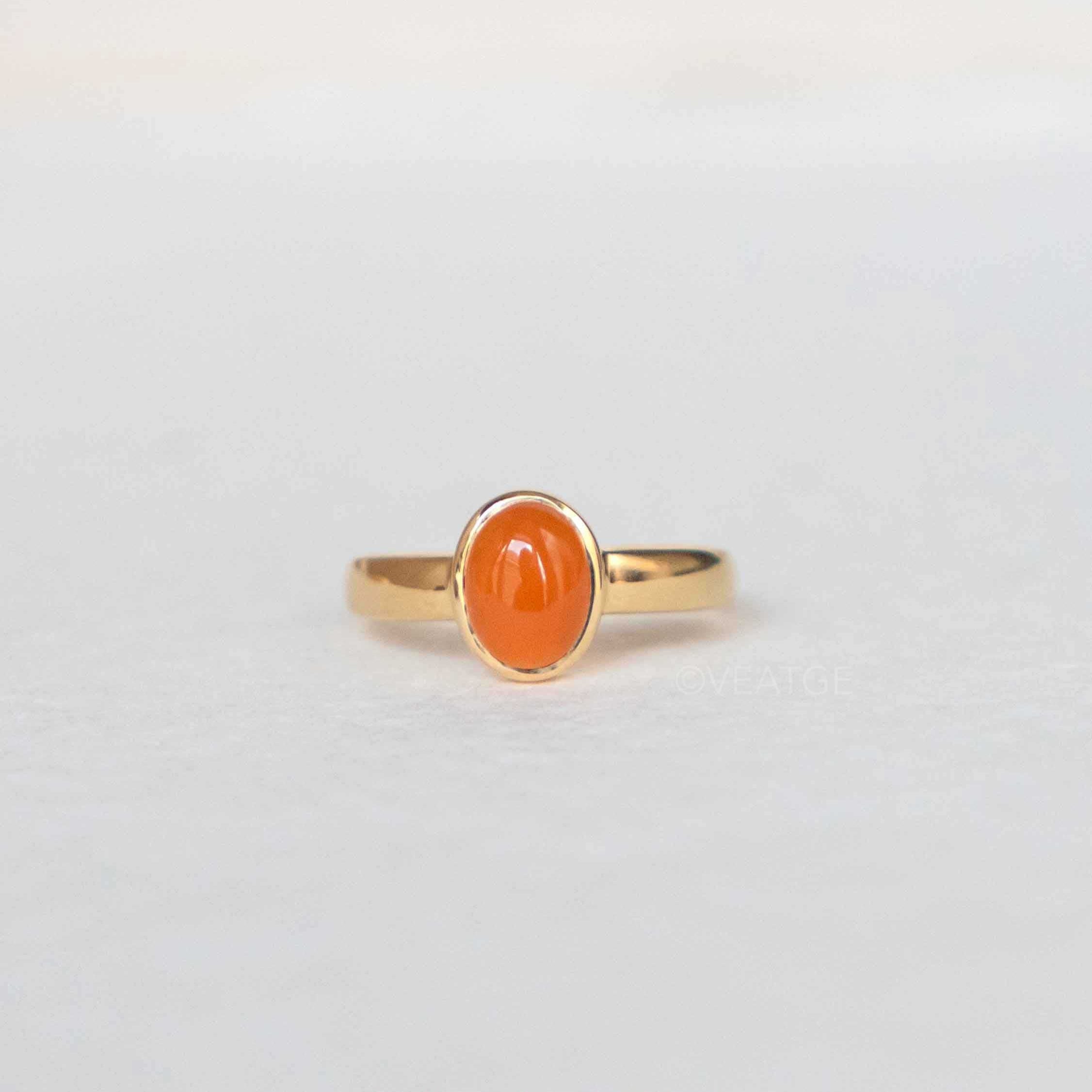 A carnelian ring with a clementine hue, set in a bezel setting on a 925 sterling silver base with a gold plating, presented on a white background with the brand name 'Veáge' visible in the corner.
