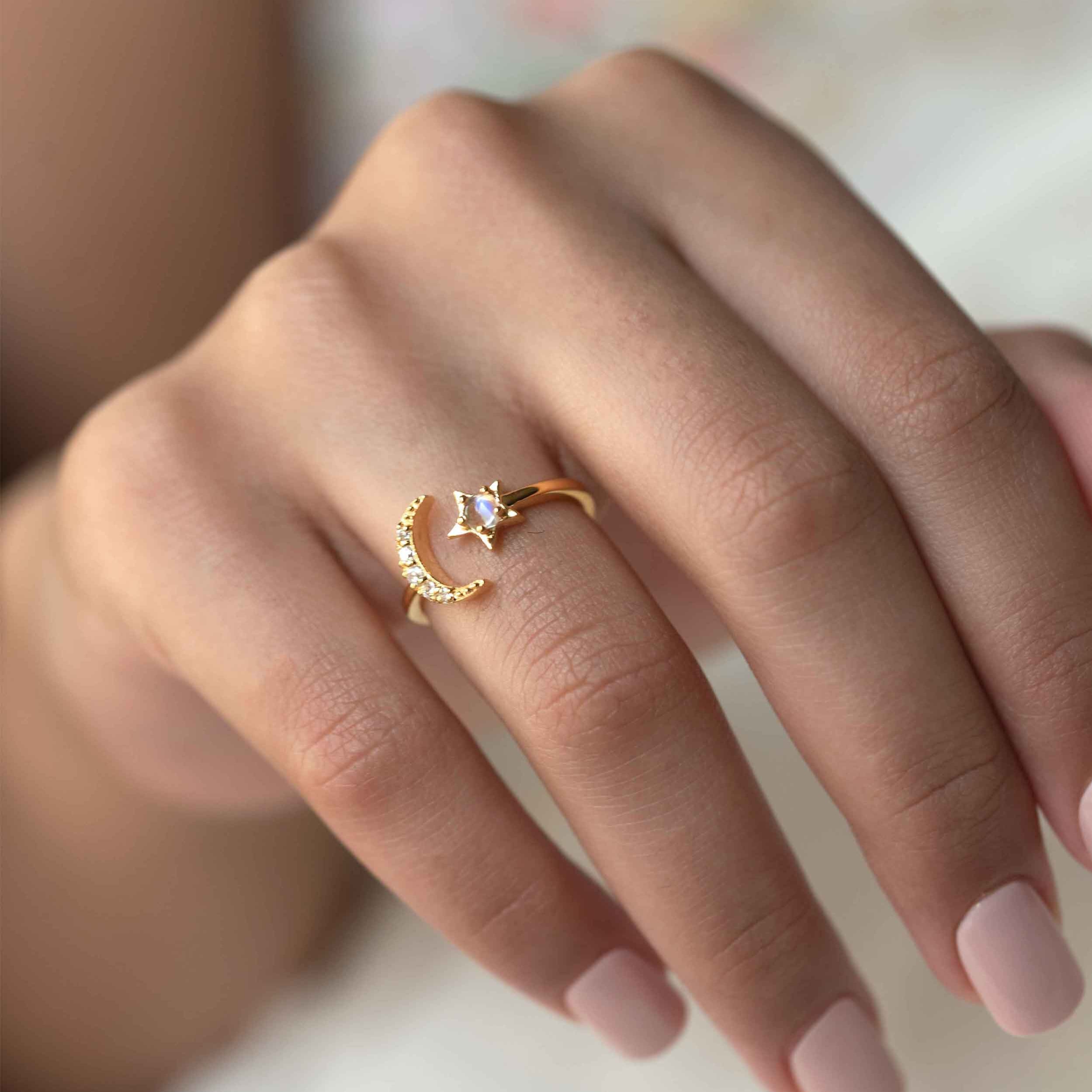 A person wearing a ring with a crescent moon and star design, featuring a blue moonstone gemstone and clear cubic zirconia.