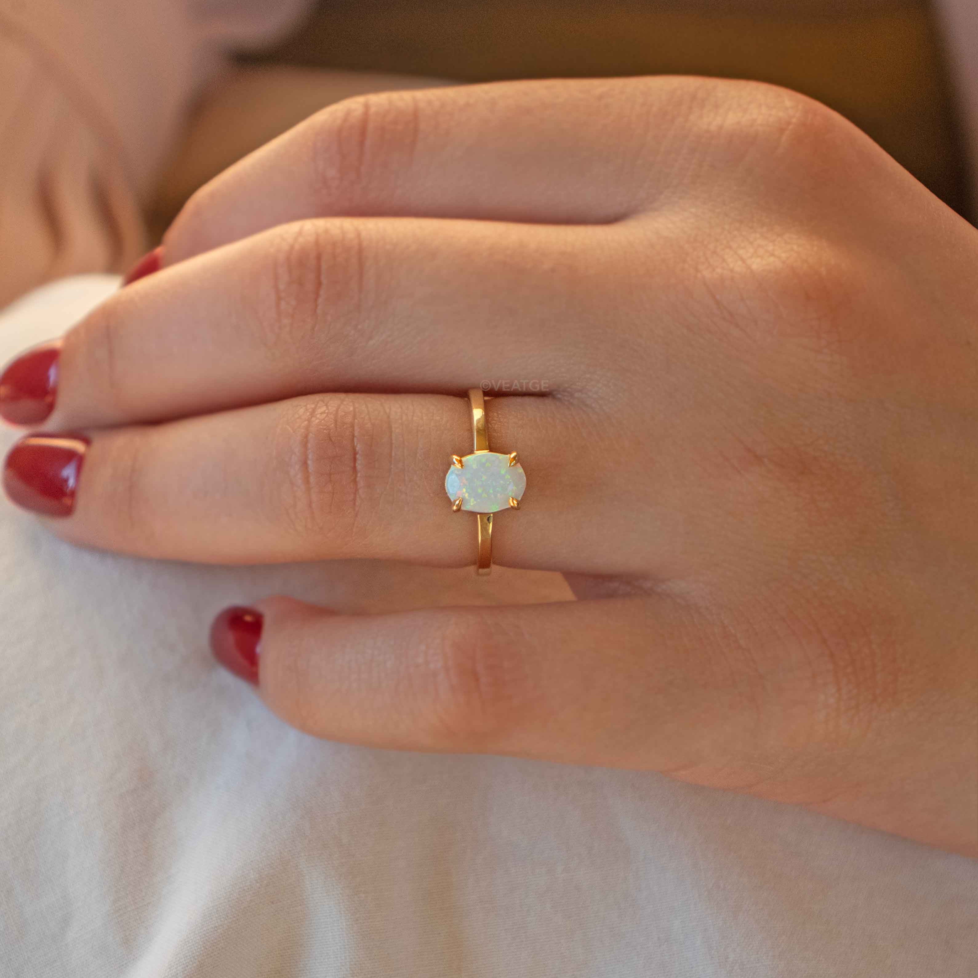A person's hand displaying a gold-colored opal ring with a sleek band, set in a white gold-colored setting.
