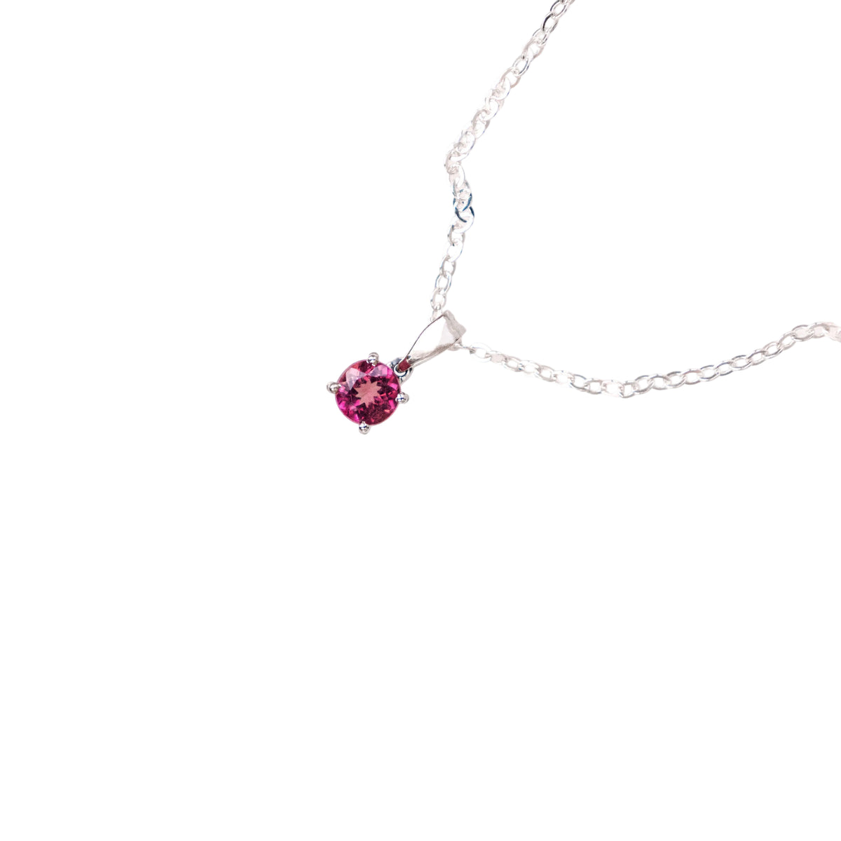 A delicate silver necklace featuring a small, round-cut pink gemstone pendant, displayed on a clean, solid off-white background.