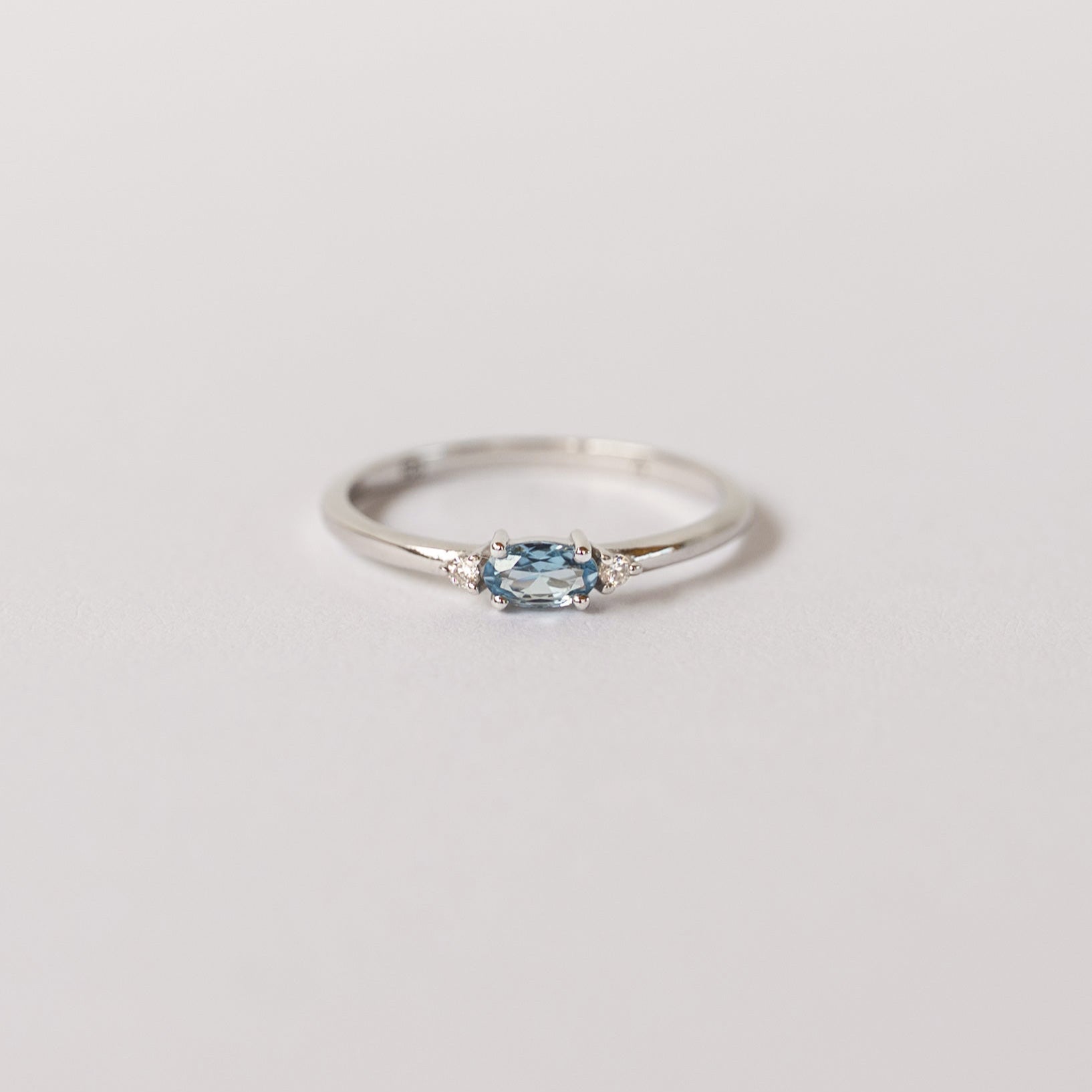 A silver dainty stacking ring with a marquise cut aquamarine center stone and two smaller clear stones on the sides, branded 'VEATGE'.