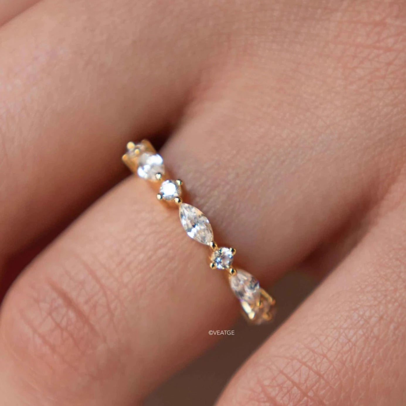 A gold-plated silver ring with marquise-shaped simulated diamonds set along its length, displayed on a person's finger.