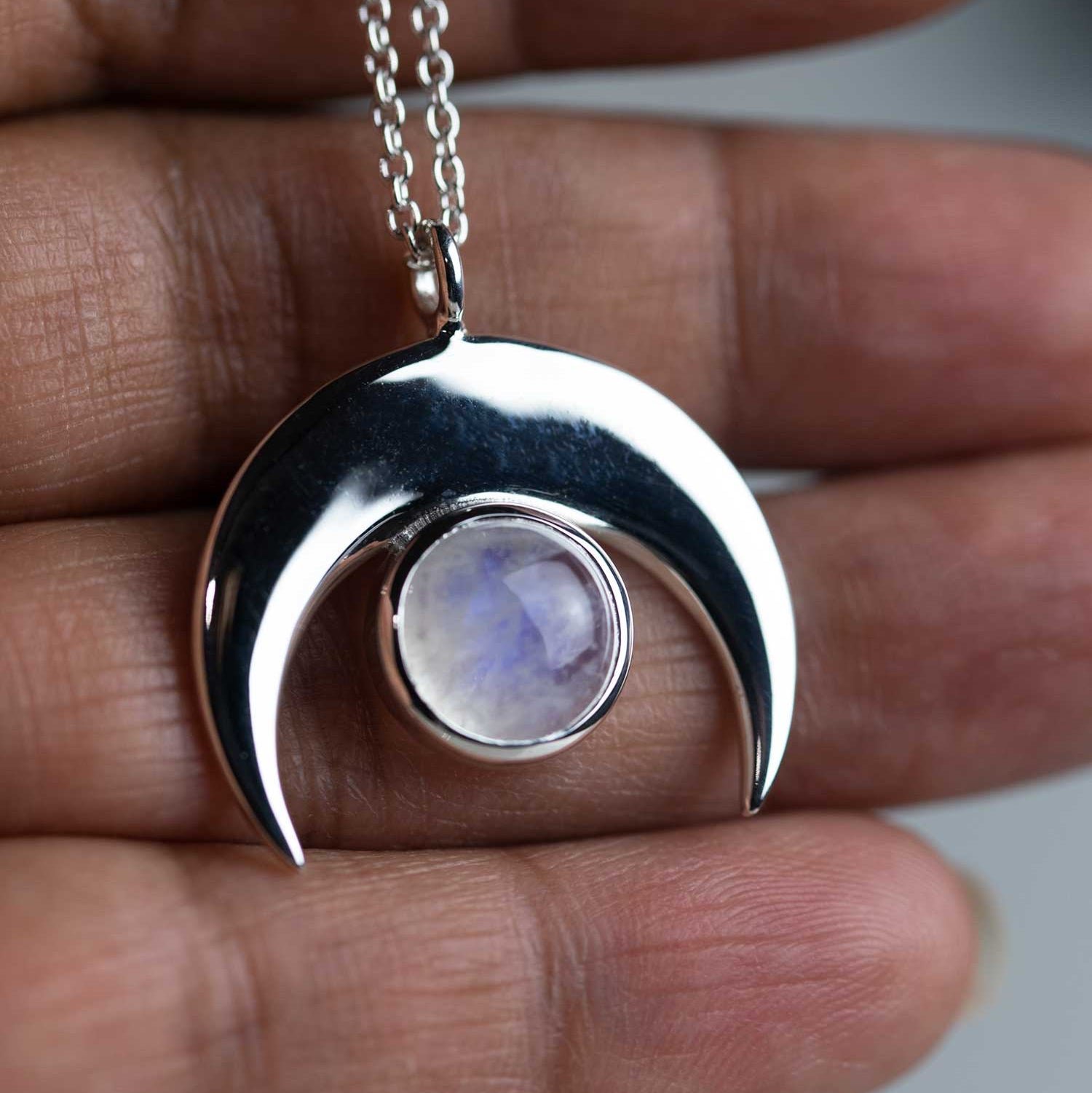 A crescent moon necklace with a moonstone in the center, held between fingers, showcasing the adjustable chain and the gold vermeil detailing.