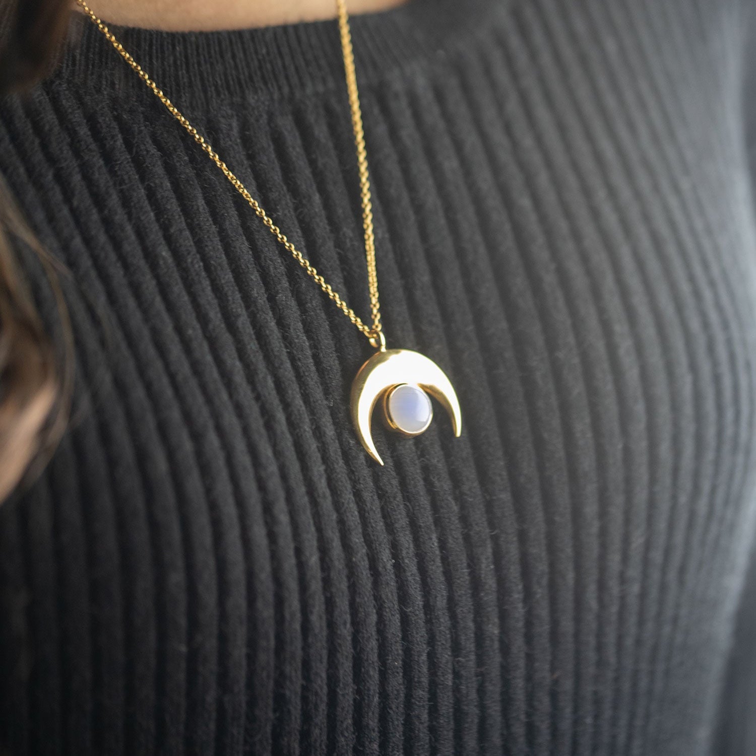 A crescent moonstone necklace with a gold vermeil finish over sterling silver, displayed on a person wearing a black top.