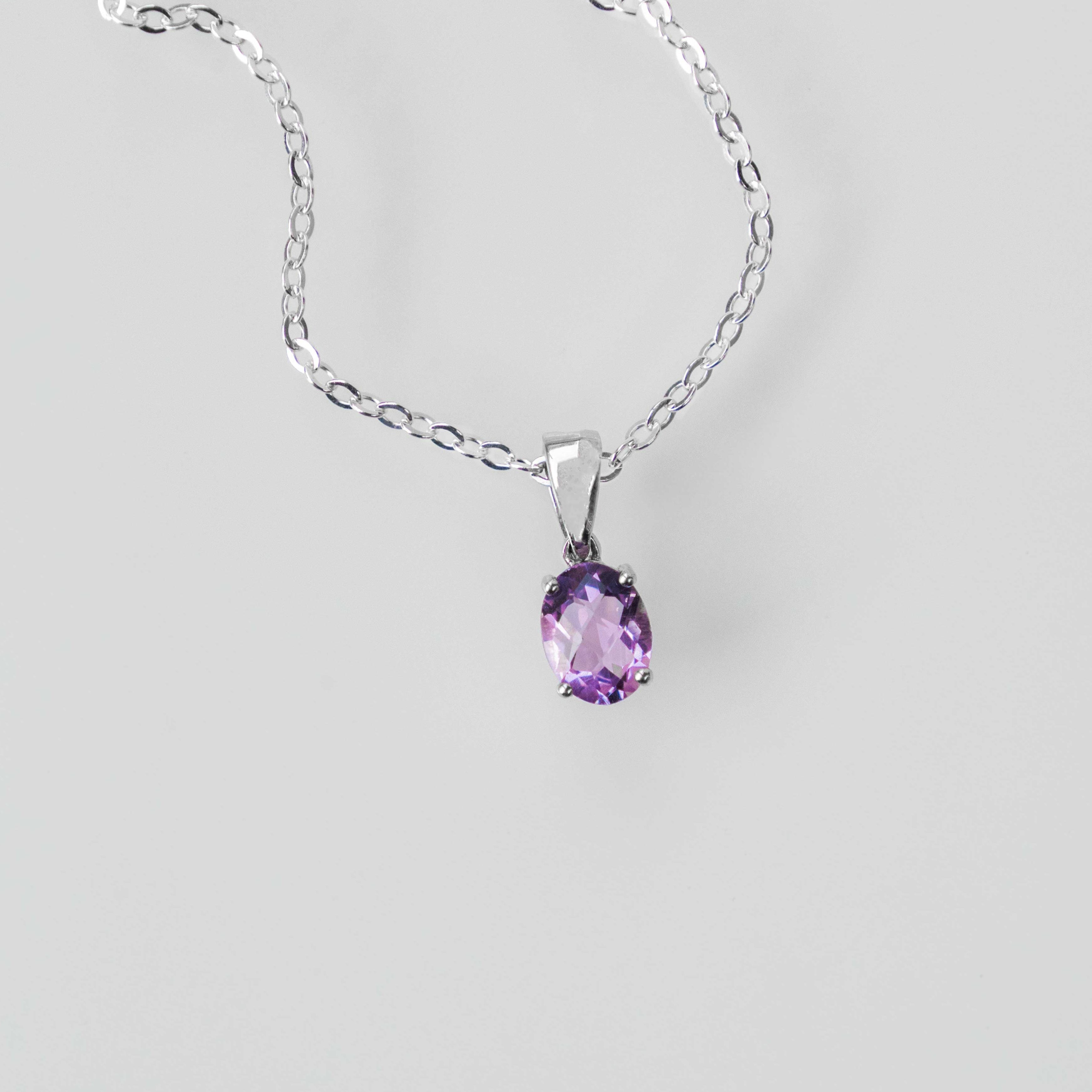 A purple amethyst gemstone in an oval four-prong setting on a silver chain.
